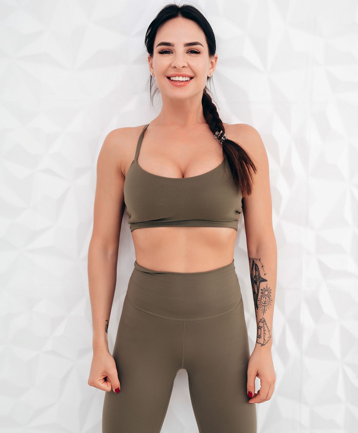 Woman in athletic wear smiling against geometric background.